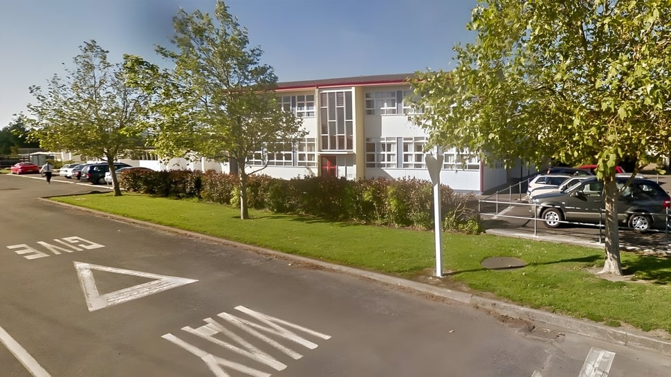 El moderno edificio de varios pisos del Kuranui College está rodeado de árboles y se encuentra en una calle con marcas viales.