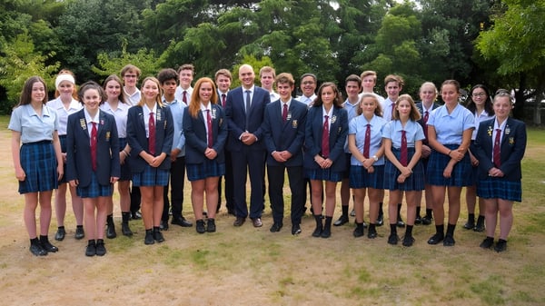 Estudiantes y profesores posan juntos en el exterior del Kuranui College frente a un fondo verde.