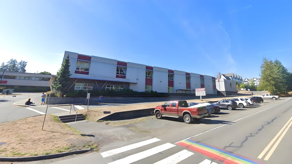 El edificio de varios pisos de la Kwalikum Secondary School con fachada rojo-blanca está rodeado de vehículos estacionados.