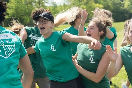 Un grupo de estudiantes de la La Lumiere School celebra y vitorea al aire libre frente a un fondo verde.