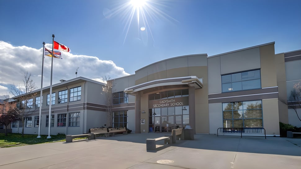El moderno edificio de varios pisos de la Ladysmith Secondary School con fachada curva y banderas alrededor bajo un brillante sol.