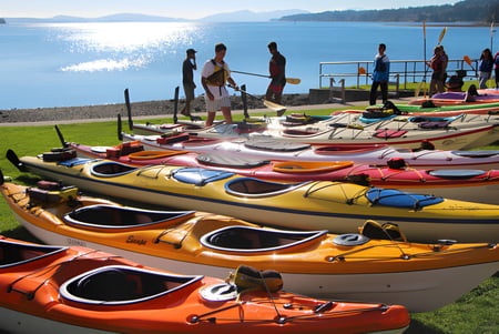 Kayaks y canoas están en la orilla de un lago en el terreno de la Ladysmith Secondary School frente a montañas.