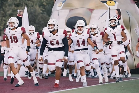 Un grupo de jugadores de fútbol americano en uniformes blancos corre hacia el campo de Lafayette Christian Academy.
