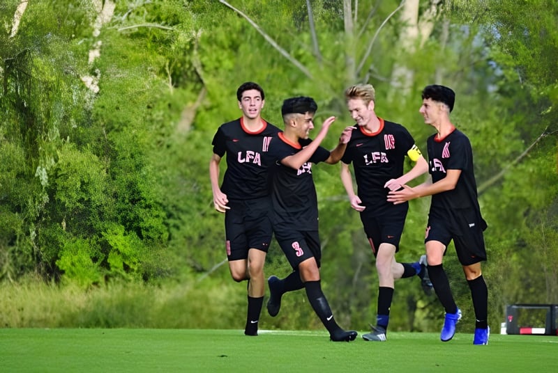Un grupo de jóvenes jugadores de fútbol de la Lake Forest Academy corre juntos sobre un campo verde con vegetación circundante.