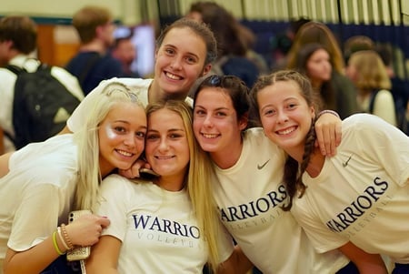 Un grupo de alumnas sonrientes en camisetas de Warriors posan juntas en la Lake George Junior-Senior High School.