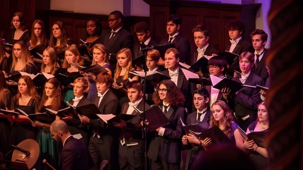 Estudiantes de la Lake Orion High School realizan una presentación musical en el escenario con ropa formal.