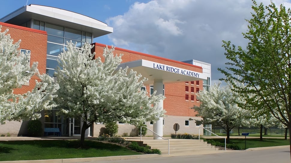El edificio de ladrillo de la Lake Ridge Academy está rodeado de árboles en flor y un césped bajo un cielo nublado.