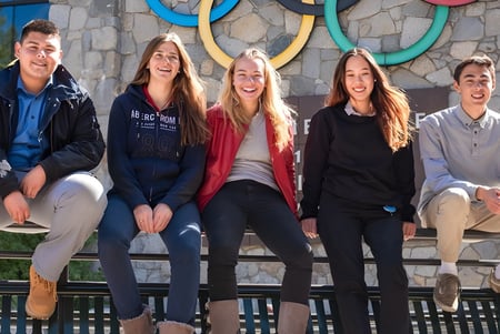 Cinco estudiantes de la Lake Tahoe Preparatory School están sentados en un banco de madera frente a una pared con patrones circulares coloridos.