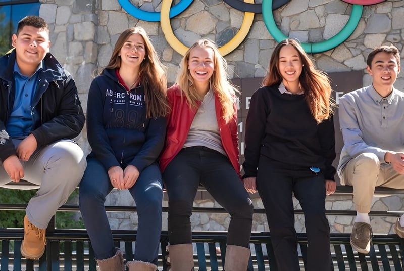 Cinco estudiantes de la Lake Tahoe Preparatory School están sentados en un banco de madera frente a una pared con patrones circulares coloridos.