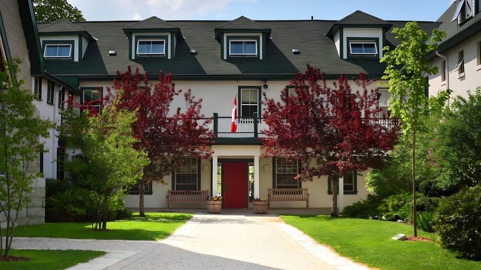 El edificio de varios pisos con techo verde de Lakefield College School está rodeado de árboles verdes y rojos.
