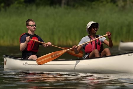 Dos estudiantes de Lakefield College School reman en un canoa en una tranquila agua rodeada de vegetación verde.