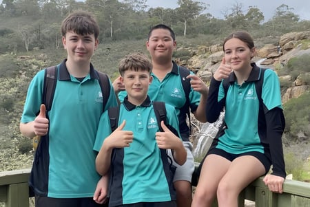 Cuatro estudiantes de la Lakeland Senior High School están juntos en un puente de madera con vista a un paisaje boscoso.