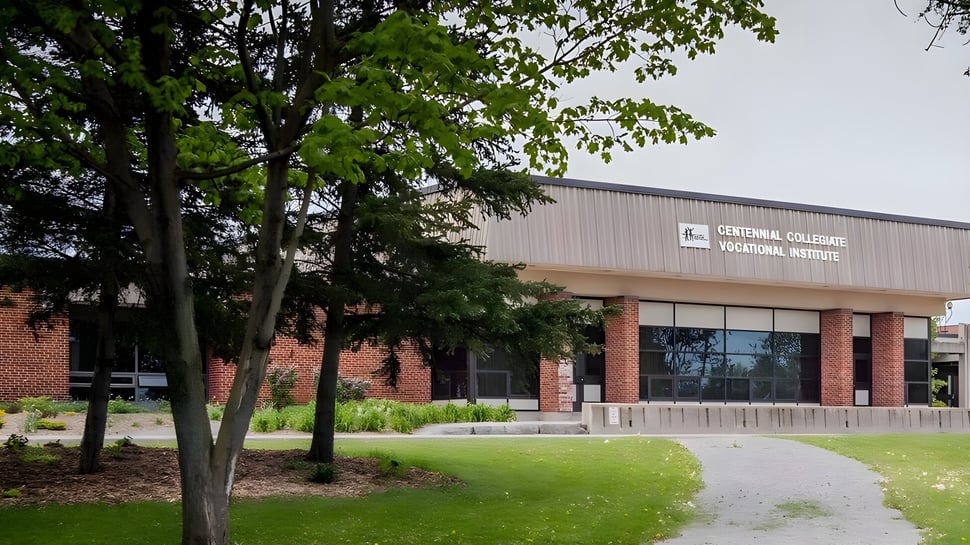 El edificio de ladrillo del Lambton Central Collegiate & Vocational School está rodeado de árboles y una zona de césped.