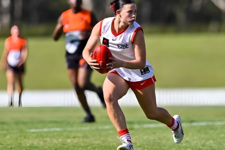 Una atleta en un traje deportivo blanco y rojo corre en el campo de deportes de la Lambton High School.