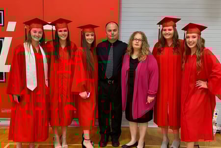 Un grupo de estudiantes de la Lambton Kent Composite School está de pie en togas rojas de graduación frente a una pared roja.