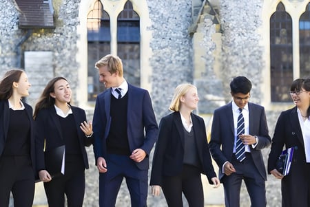 Un grupo de estudiantes del Lancing College pasa frente a un edificio histórico de piedra con ventanas de arco.