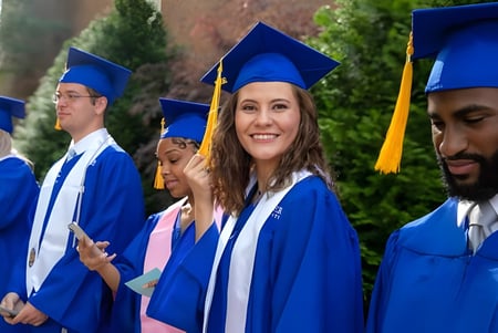 Un grupo de graduados de Lander University está junto con togas azules frente a un fondo verde.