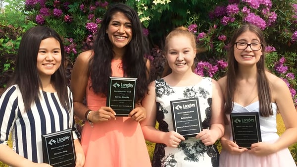 Cuatro estudiantes de la Langley Fine Arts School están juntas en un jardín con flores rosas de fondo.
