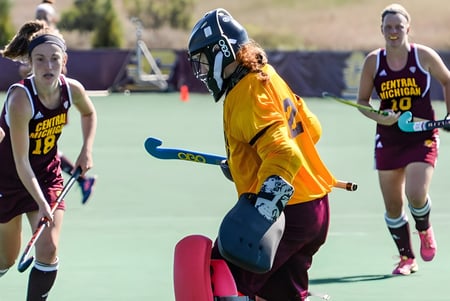 Estudiantes de la Langley School juegan al hockey sobre campo en el campo deportivo con un jugador en uniforme amarillo en primer plano.