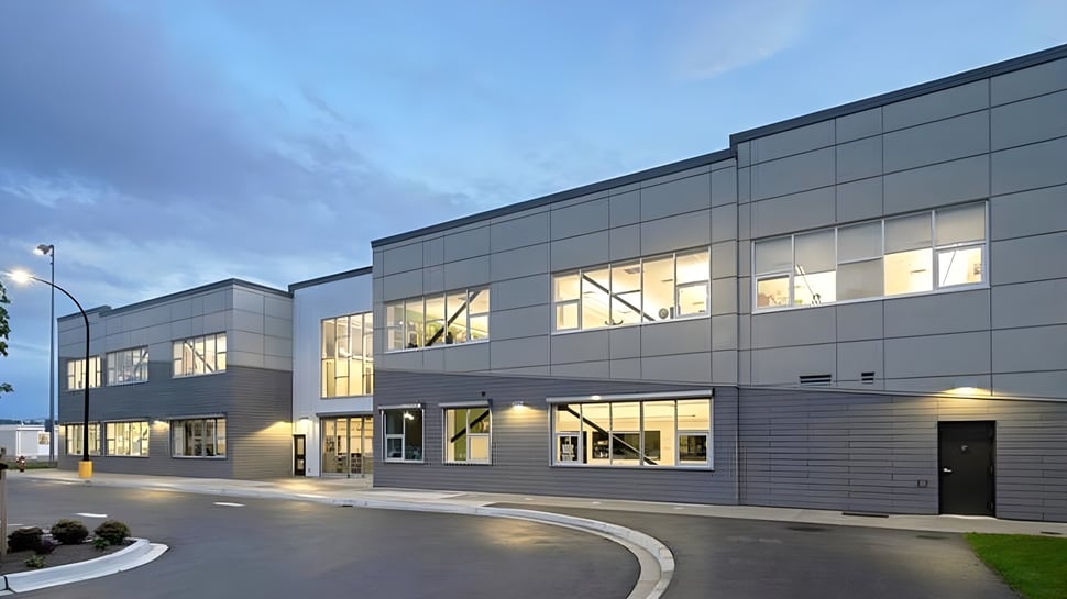 El moderno edificio escolar de la Langley Secondary School con grandes ventanas y una entrada curva bajo un cielo nublado.