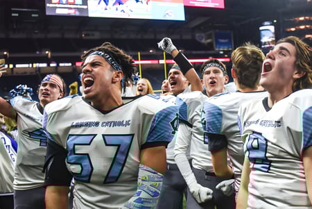 Los estudiantes de Lansing Catholic High School celebran juntos en el campo de fútbol frente al marcador y la iluminación del estadio.