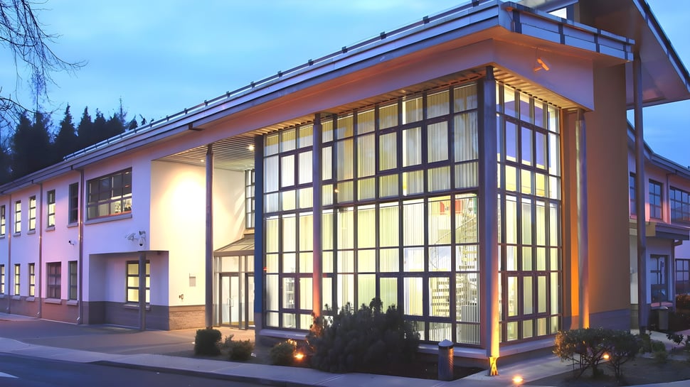 El edificio moderno con fachada de vidrio y techo inclinado de Largy College se encuentra en una zona boscosa y está iluminado por la noche.