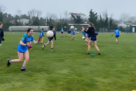Un grupo de estudiantes del Largy College juega un partido en un campo de césped con árboles y edificios de fondo.
