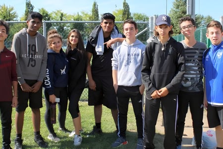 Un grupo de estudiantes está de pie en un campo verde frente a edificios en el campus de LaSalle Community Comprehensive High School.