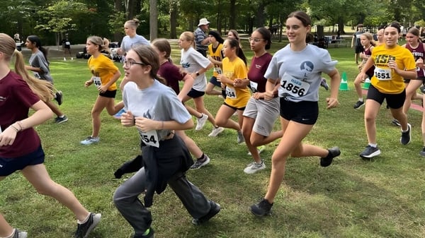Un grupo de estudiantes de LaSalle Community Comprehensive High School participa en una competencia de carrera en un campo cubierto de hierba.