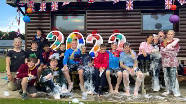 Un grupo de estudiantes de la Lathallan School se reúne frente a una cabaña de madera con banderas del Union Jack después de una colorida actividad festiva.