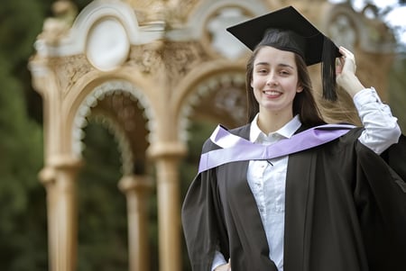 Una graduada sonriente en toga y birrete se encuentra frente a un fondo arquitectónico en Launceston College.