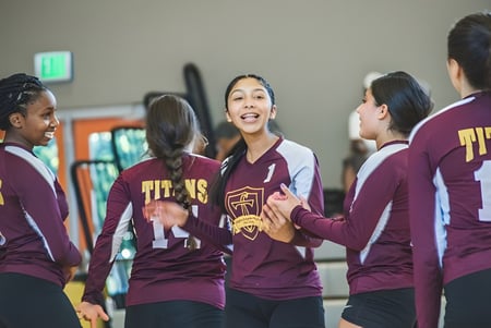 Un grupo de estudiantes de la LaurenHill Academy está en uniforme deportivo en un gimnasio y conversan entre sí.
