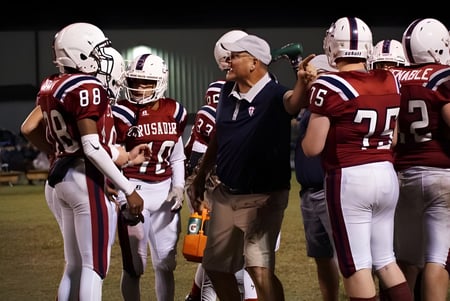 Estudiantes y un entrenador de la Laurens Academy están en uniforme de fútbol en un campo de juego por la noche.