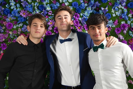 Tres estudiantes de la Layton Christian Academy posan juntos frente a un colorido fondo de flores.