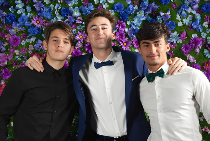 Tres estudiantes de la Layton Christian Academy posan juntos frente a un colorido fondo de flores.