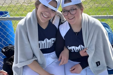 Dos alumnas sonrientes de la École secondaire publique Le Sommet están frente a una cerca con un contenedor azul de fondo.