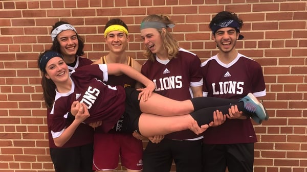 Un grupo de estudiantes en camisetas maroon de los Lions posan frente a una pared de ladrillo en el terreno de la Leamington District Secondary School.