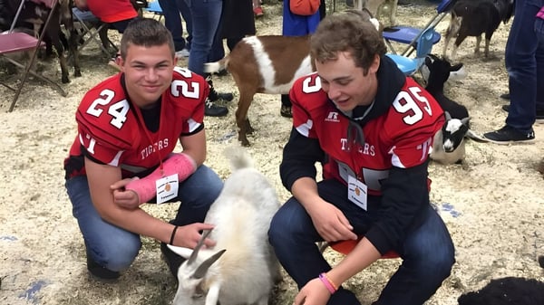 Dos estudiantes de Leduc Composite High School están sentados en el suelo e interactuando con un pequeño perro blanco.