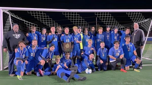 Estudiantes de Lee Academy celebran en el campo de fútbol su victoria y sostienen un trofeo.