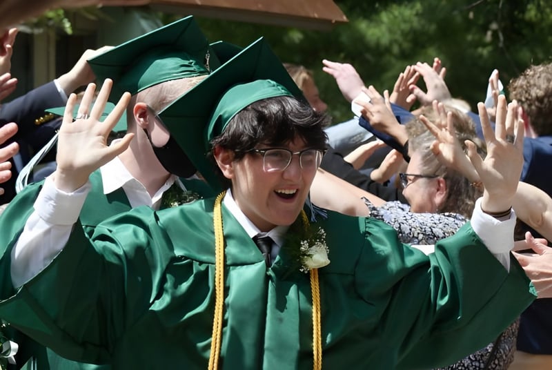 Los graduados de la Leelanau School celebran en sus togas verdes y levantan las manos en una ceremonia de graduación.