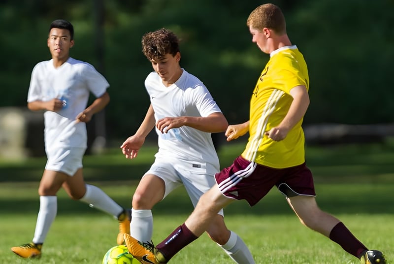 Tres estudiantes de la Léman Manhattan Preparatory School juegan al fútbol en un campo deportivo verde.
