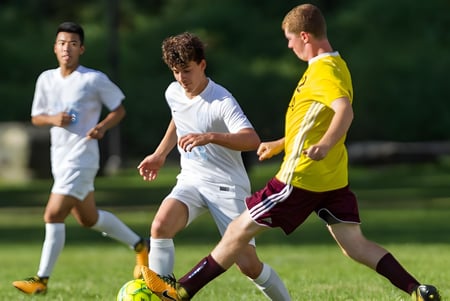 Tres estudiantes de la Léman Manhattan Preparatory School juegan al fútbol en un campo cubierto de hierba.