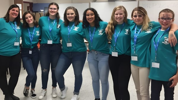 Un grupo de alumnas con camisetas verdes están juntas en un edificio escolar de la Leo Burke Academy.