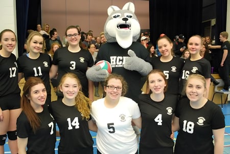 Un grupo de jóvenes deportistas de la Leo Burke Academy posan junto con la gran mascota blanca en el gimnasio.