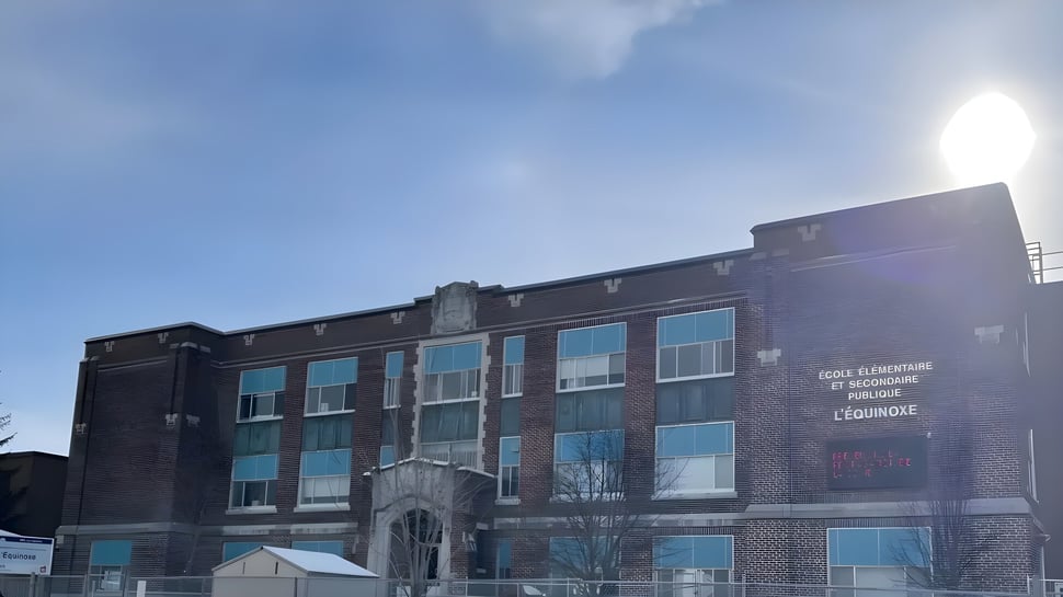 El edificio de ladrillo de varios pisos de la École élémentaire et secondaire publique L'Équinoxe con grandes ventanas bajo un cielo azul.