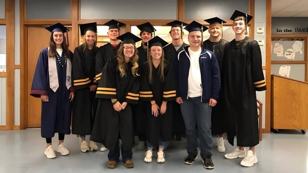 Un grupo de graduadas y graduados en la vestimenta de graduación en el campus de la Lester B. Pearson Catholic High School.