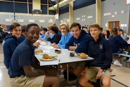 Estudiantes de la Liberty Christian Academy están juntos en la mensa comiendo una comida bajo aros de baloncesto.
