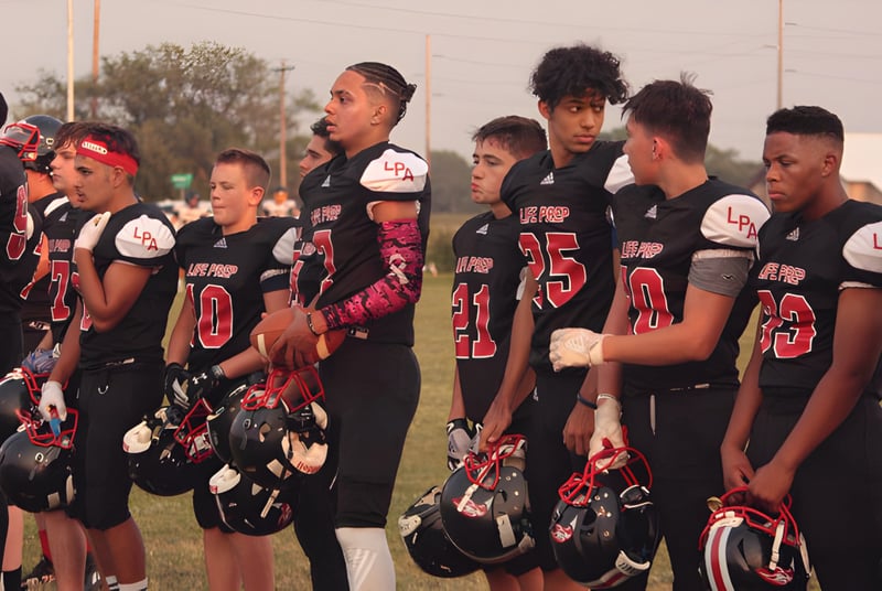 Un grupo de jóvenes atletas está reunido en el campo de deportes de la Life Prep Academy.