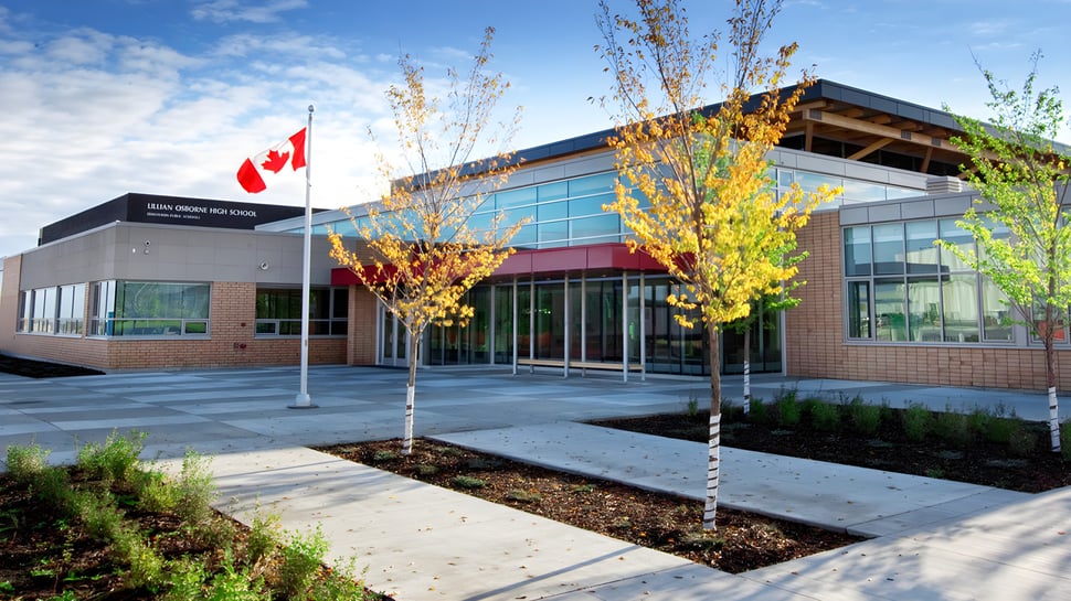 El moderno edificio de la Lillian Osborne High School con bandera canadiense y árboles de colores otoñales en el entorno.