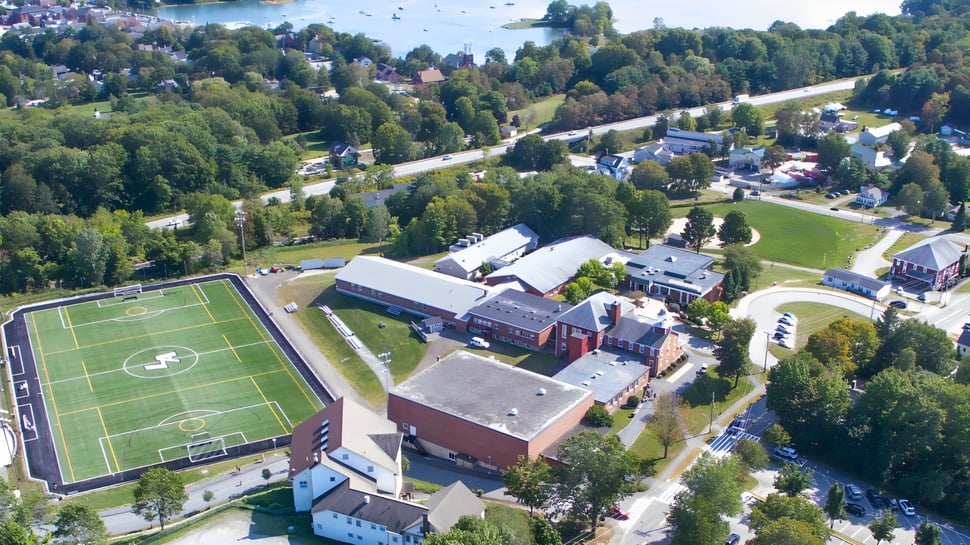 Vista aérea de la Lincoln Academy con campo de deportes y edificios rodeados de bosques verdes.
